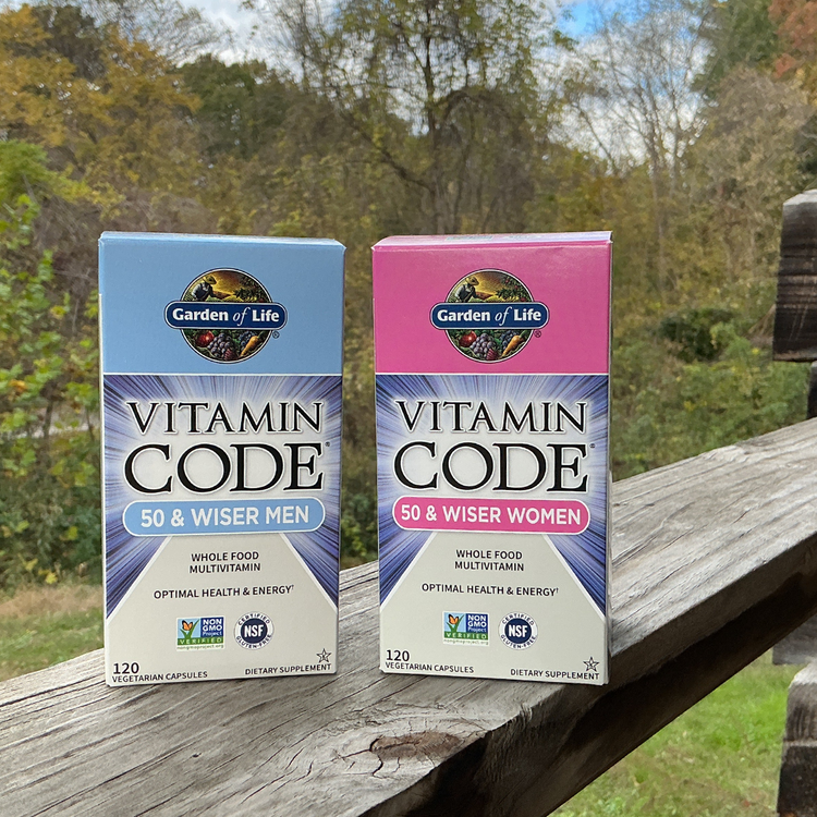 Two Garden of Life Vitamin Code supplement boxes on a wooden surface with a natural background.