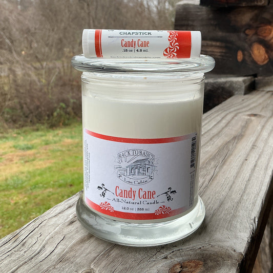 Candle in a glass jar with a red and white label on a wooden surface outdoors.
