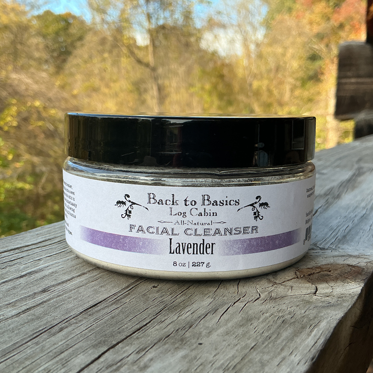 Facial cleanser jar labeled 'Back to Basics Log Cabin' on a wooden surface with a natural background