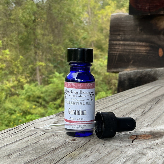 A small cobalt blue glass bottle of essential oil with a black dropper cap, standing on a weathered wooden ledge with a log cabin wall and green forest in the background.