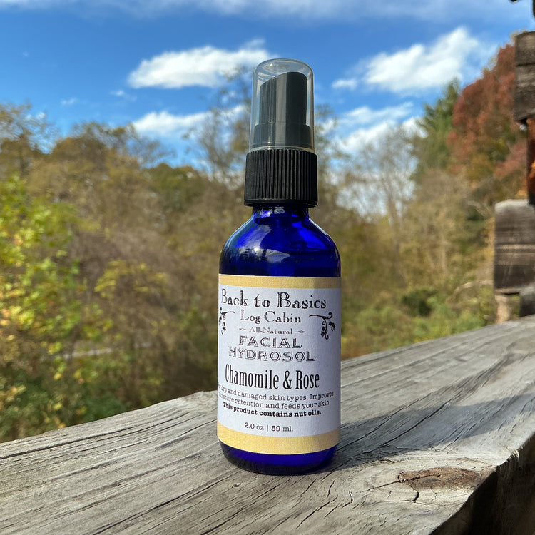 Bottle of 'Back to Basics Log Cabin' Chamomile & Rose Hydrosol on a wooden surface with a natural background