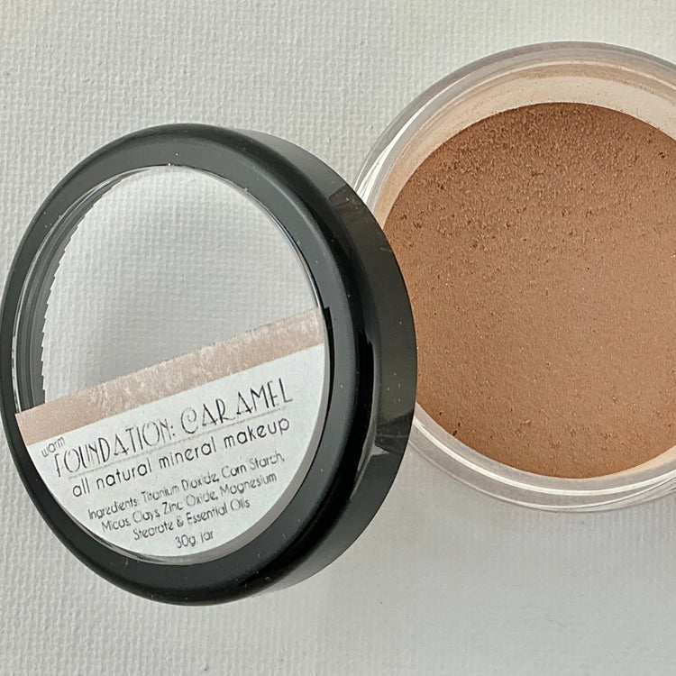 Open container of foundation powder with a mirror on a light gray background
