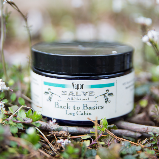 Jar of 'Back to Basics Log Cabin' salve on a wooden surface with a natural background