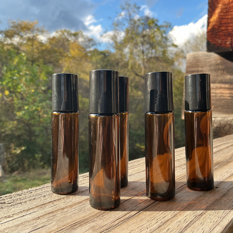 Set of five amber glass roller bottles with black caps on a wooden surface outdoors.