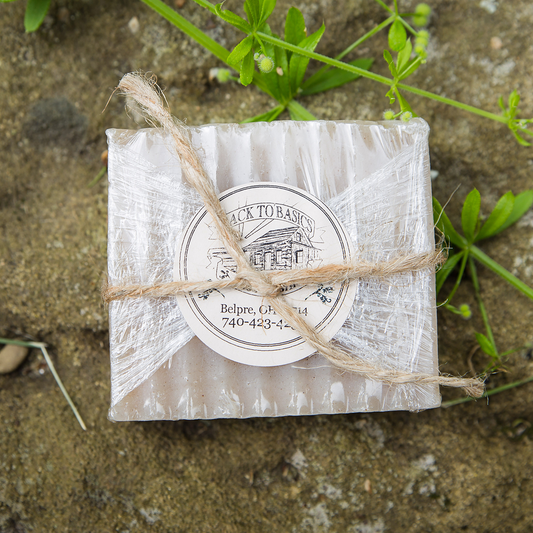 Bar of soap wrapped in paper with twine, placed on a natural background with greenery.