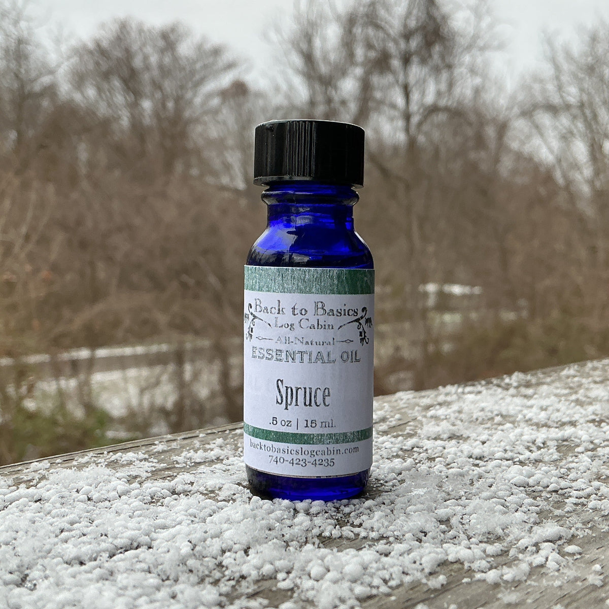 Bottle of essential oil labeled 'Spruce' on a wooden surface with snowflakes.