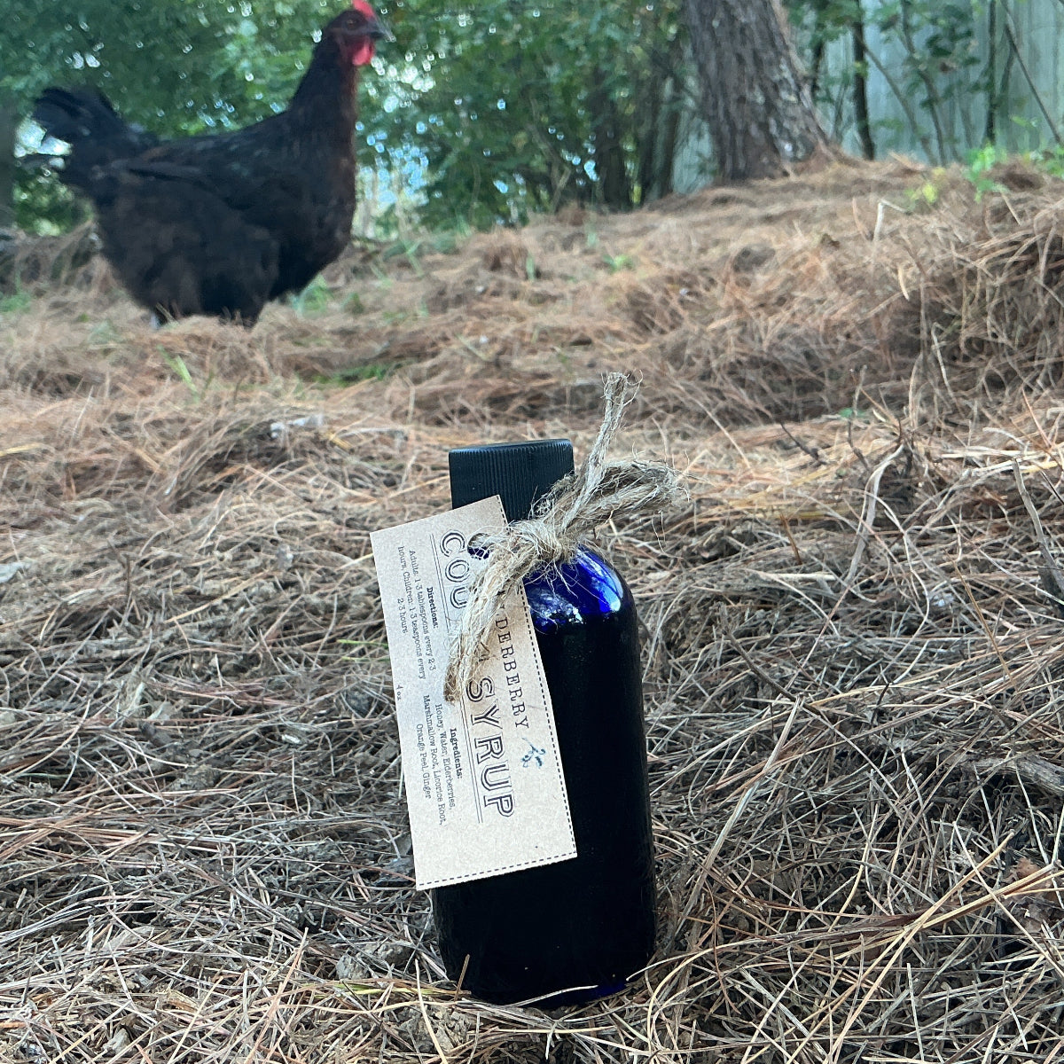 Bottle of 'Rippling C' with a chicken in the background on a natural setting