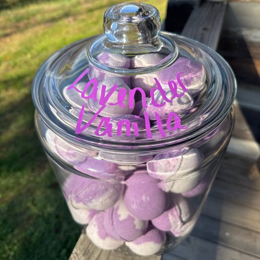 Clear jar with purple and white spherical objects inside, labeled 'Lavender Vanilla', on a wooden surface.