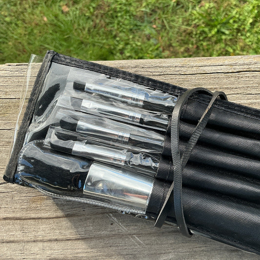 Set of makeup brushes in a black case on a wooden surface with grass in the background