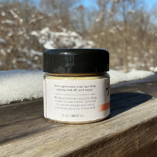 Small jar with a black lid on a wooden surface outdoors with snow and trees in the background