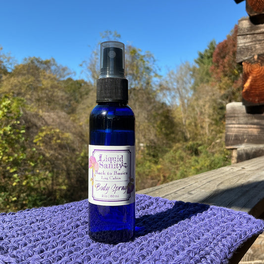 Blue spray bottle labeled 'Liquid Saints' on a purple cloth with a wooden bench and trees in the background