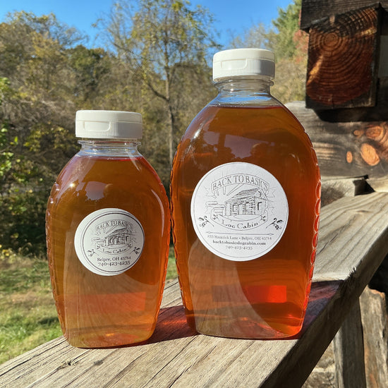 Two bottles of honey with labels on a wooden surface outdoors.