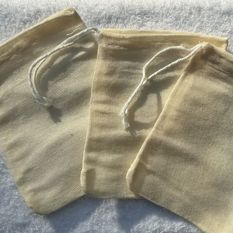 Three beige drawstring bags on a textured surface with a blurred natural background