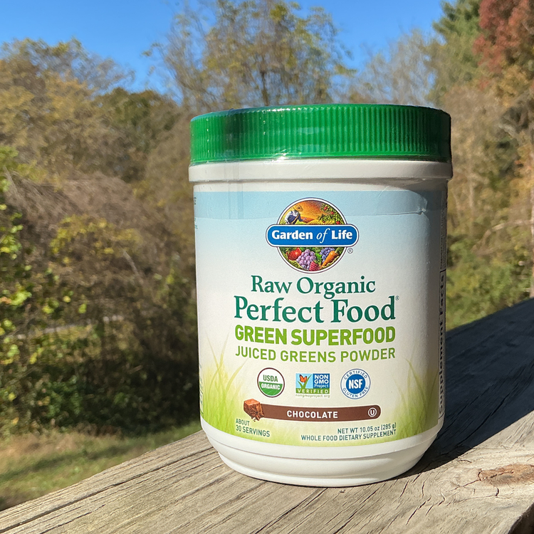 Garden of Life Raw Organic Perfect Food Green Superfood container on a wooden surface with trees in the background