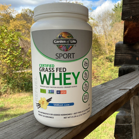 Garden of Life Sport Certified Grass Fed Whey protein powder container on a wooden surface with a natural background.