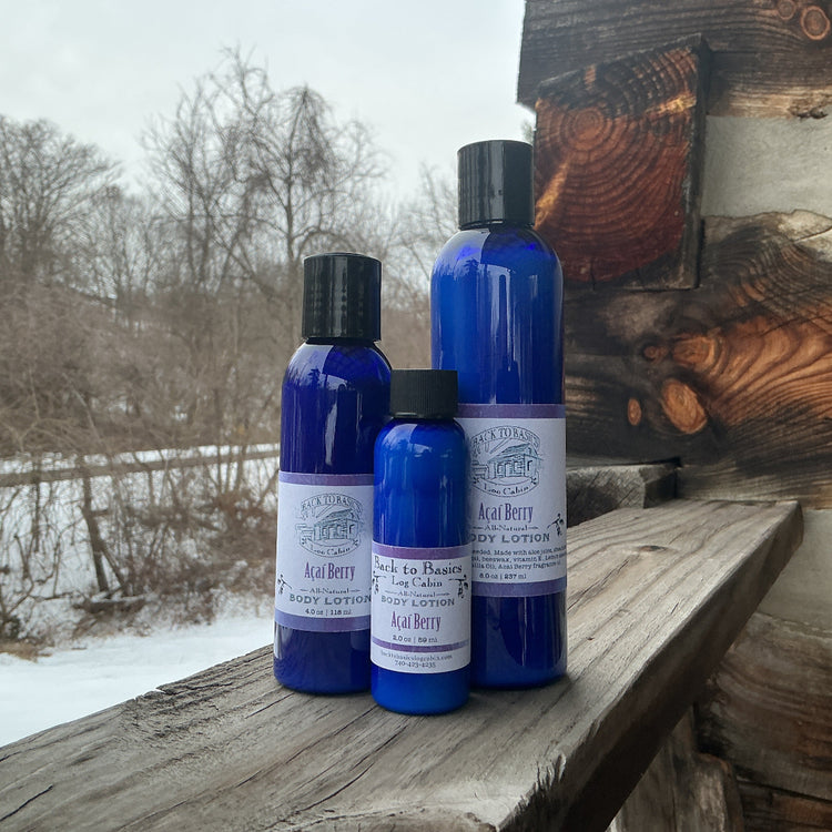 Three blue bottles with labels on a wooden surface outdoors with snow and trees in the background