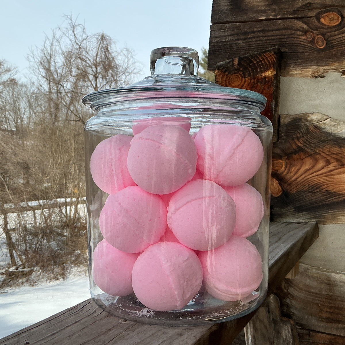 Glass jar filled with pink bath bombs on a wooden surface with a snowy landscape in the background.