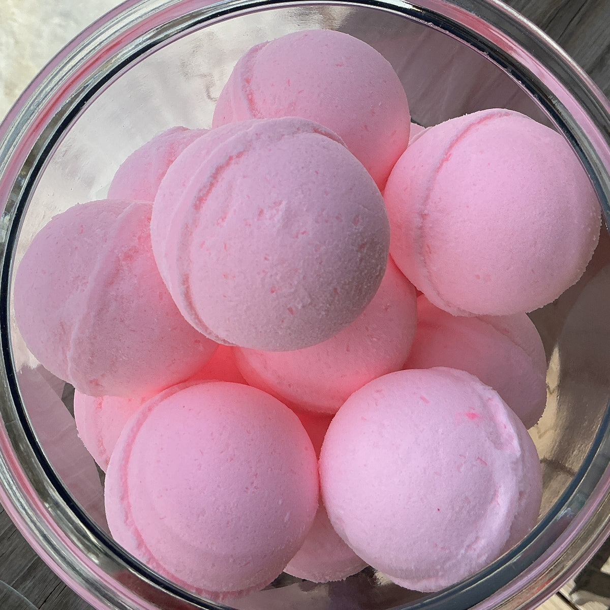 Glass bowl filled with pink bath bombs on a wooden surface.
