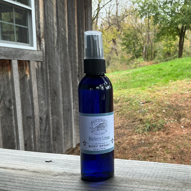 Blue bottle of body spray with a label on a wooden surface outdoors.