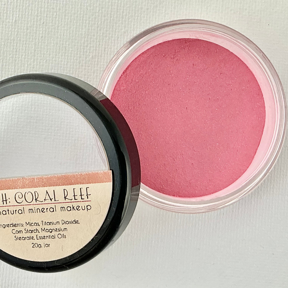 Open container of blush with visible pink color on a light gray background