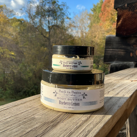 Two jars of body butter stacked on a wooden surface with a natural outdoor background