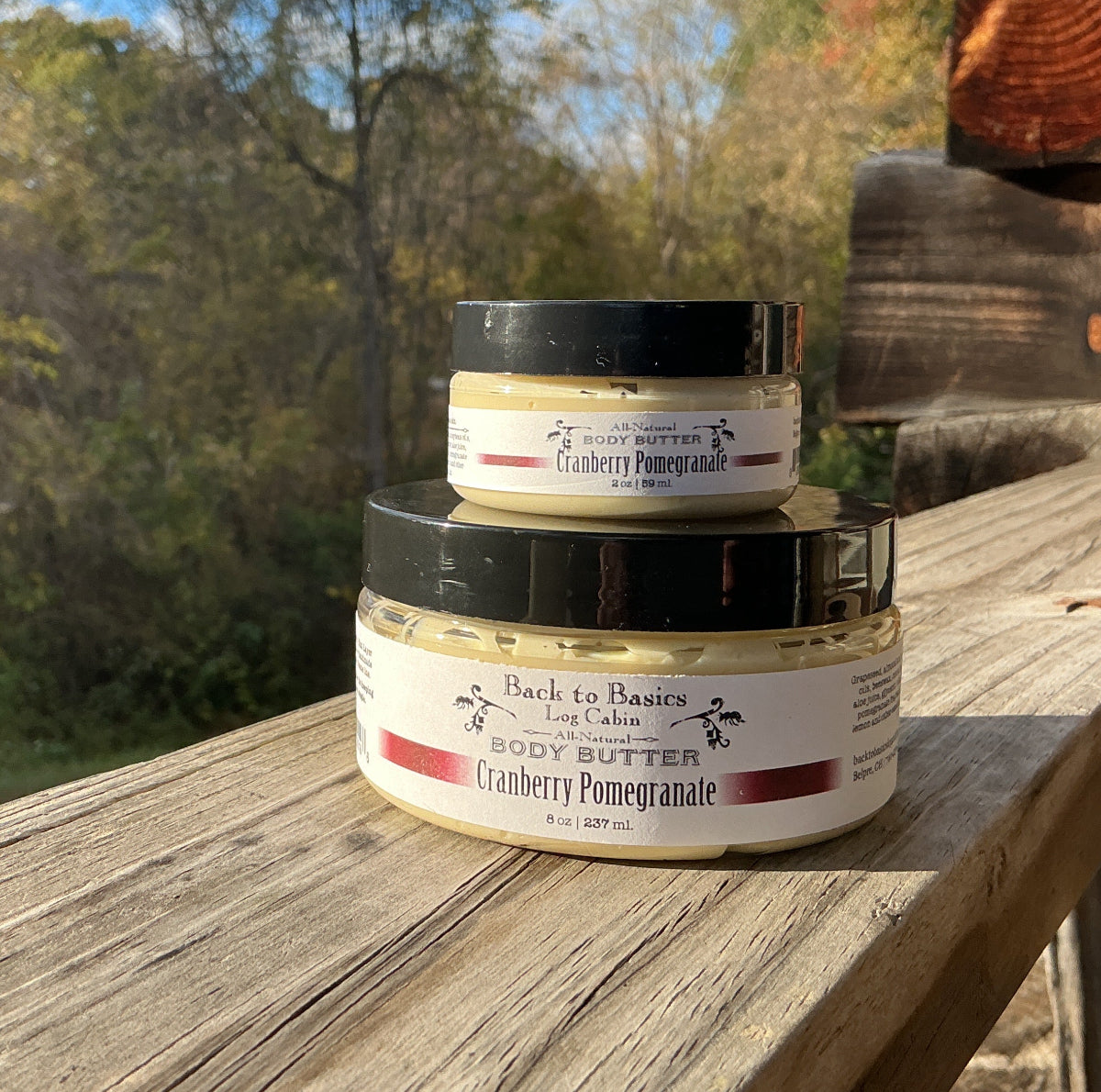 Three jars of body butter stacked on a wooden surface with a natural outdoor background