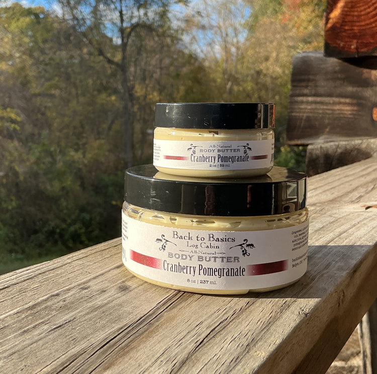 Three jars of body butter stacked on a wooden surface with a natural outdoor background
