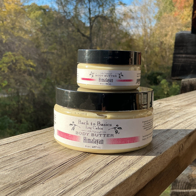 Three jars of body butter stacked on a wooden surface with a natural background