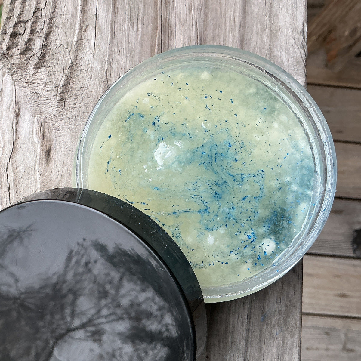 Bowl with greenish contents and black lid on a wooden surface outdoors