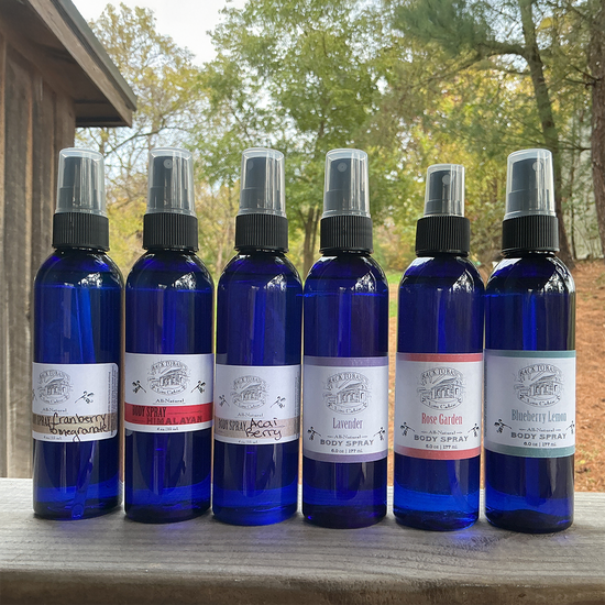 Six blue spray bottles with labels on a wooden surface outdoors.