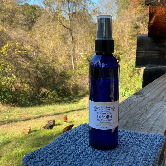 Blue spray bottle labeled 'Bug Repellent' on a wooden surface with a natural background