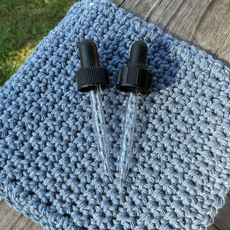 Two black droppers on a blue knitted fabric with grass and wooden surface in the background.