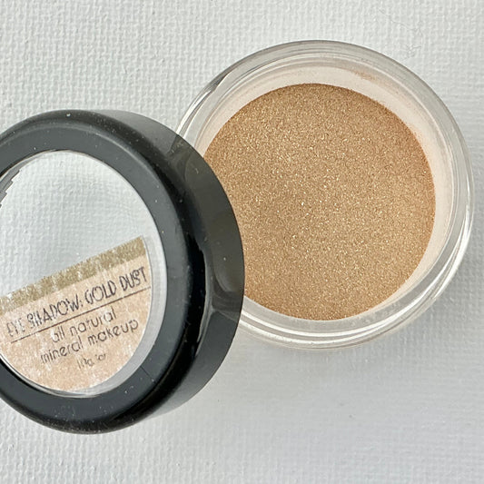 Open container of gold eyeshadow on a light gray background