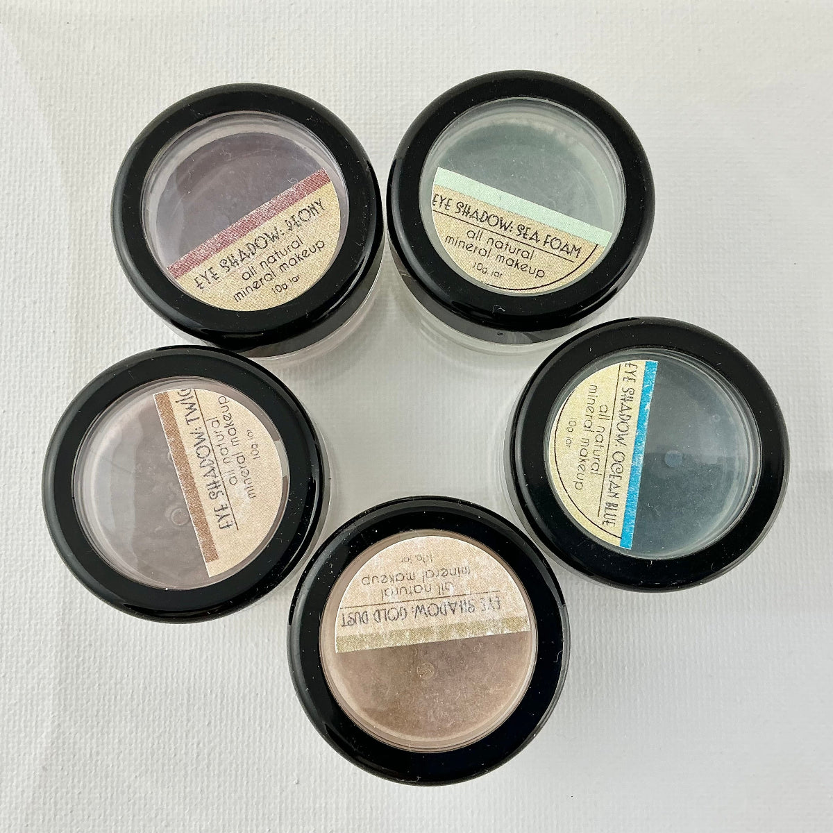 Five small makeup containers with labels on a light background