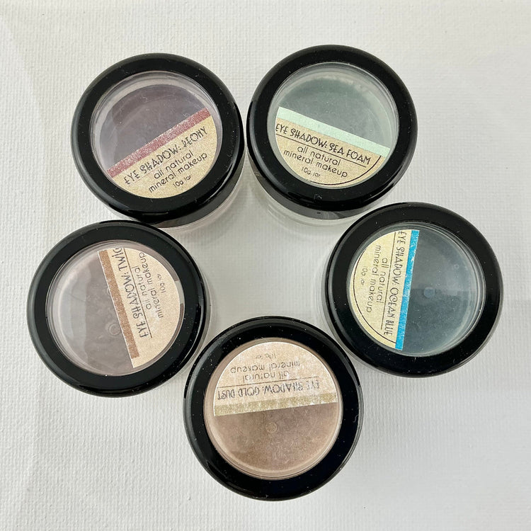 Five small makeup containers with labels on a light background