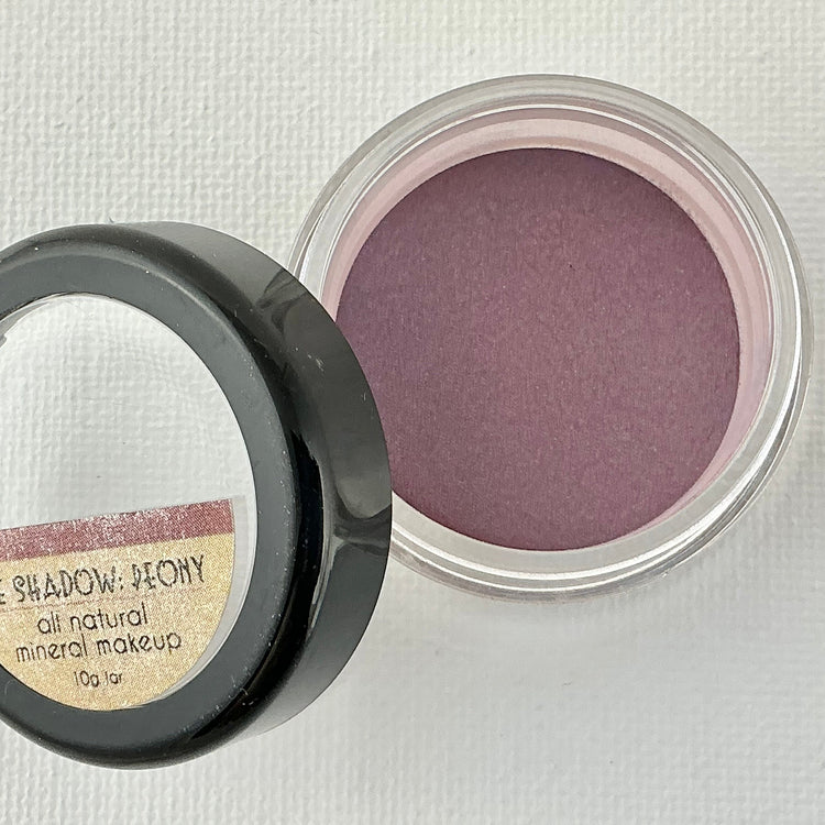 Open container of purple eye shadow with a mirror on a light gray background