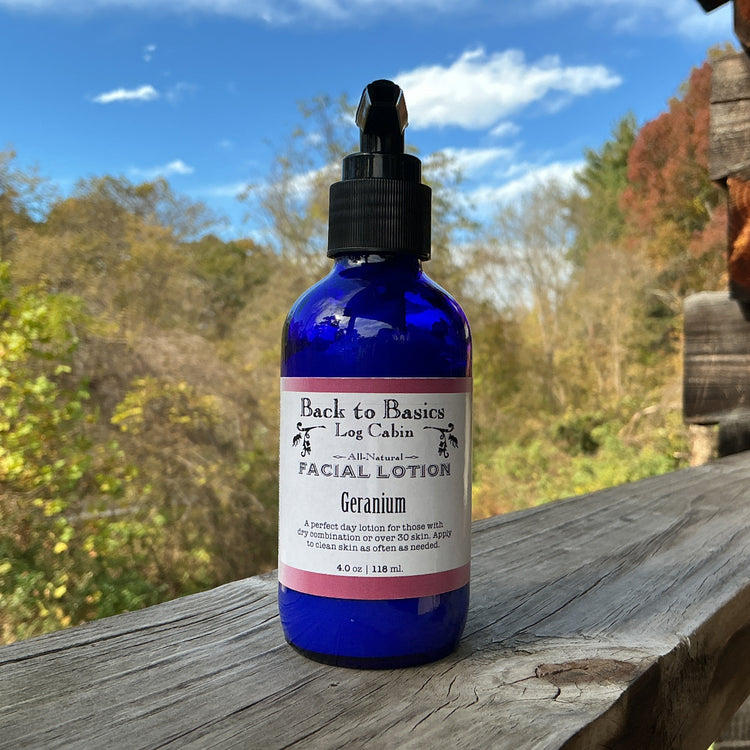 Blue bottle of facial lotion labeled 'Back to Basics Log Cabin' on a wooden surface with a scenic background.