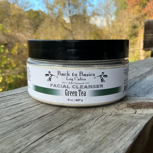 Facial cleanser jar labeled 'Back to Basics Log Cabin' on a wooden surface with a natural background