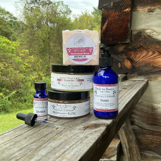 A collection of natural skincare products from Back to Nature Shop arranged on a rustic wooden porch with a green forest background. The products include a blue bottle of facial lotion, a blue dropper bottle, a jar of rosemary mask, a jar of body butter, and a bar of soap.
