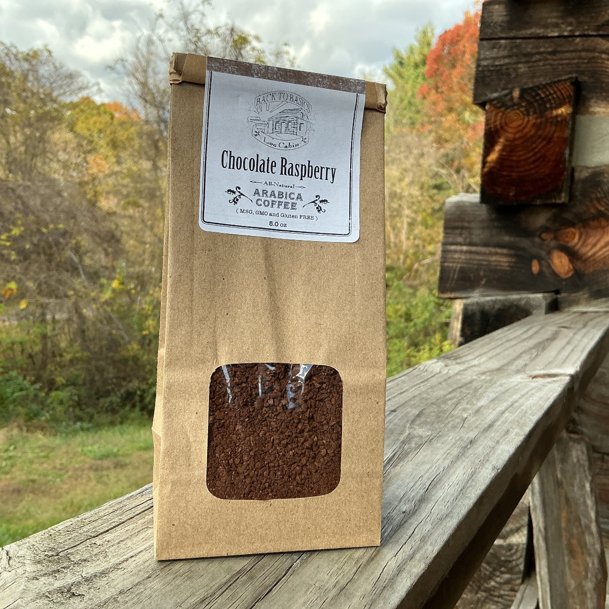 Kraft paper coffee bag with a window showing coffee beans, labeled 'Chocolate Raspberry', on a wooden surface with a natural background.