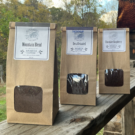 Three coffee bags with window panels on a wooden surface outdoors.