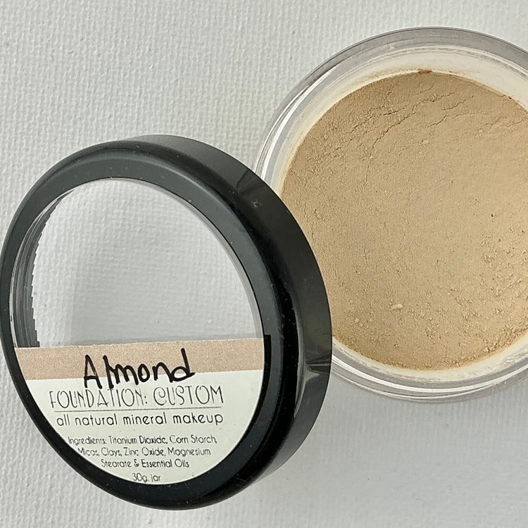 Almond foundation container with open lid on a light gray background