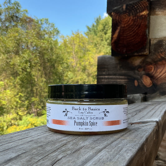 A jar of Back to Nature Co. Sea Salt Scrub in Pumpkin Spice scent, placed on a rustic wooden railing with a natural forest background.