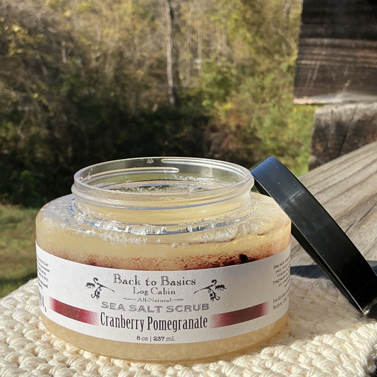Jar of cranberry pomagranate sea salt scrub with a black spoon on a wooden surface outdoors.