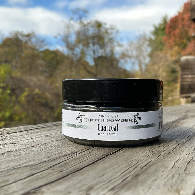 Jar of charcoal tooth powder on a wooden surface with a natural background